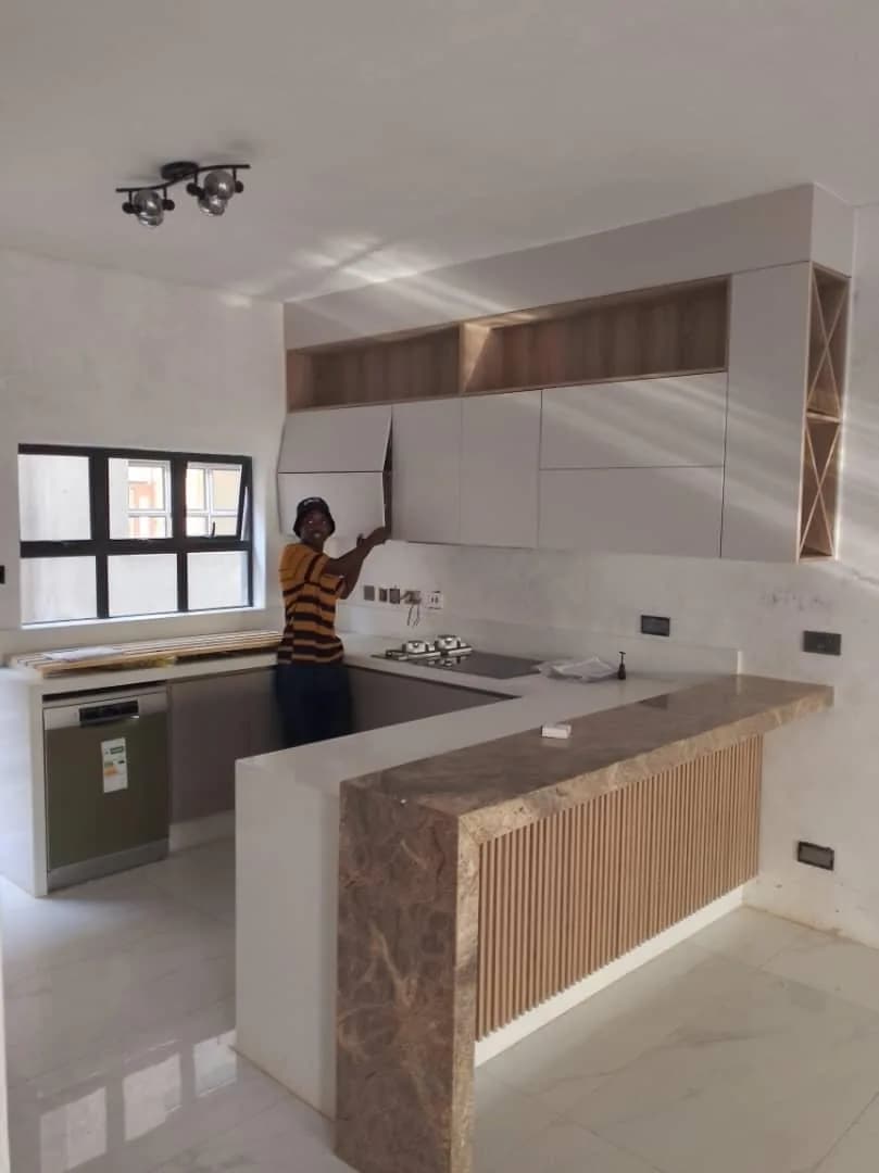 Installer fitting wall units in a new kitchen with a timber-slatted counter
