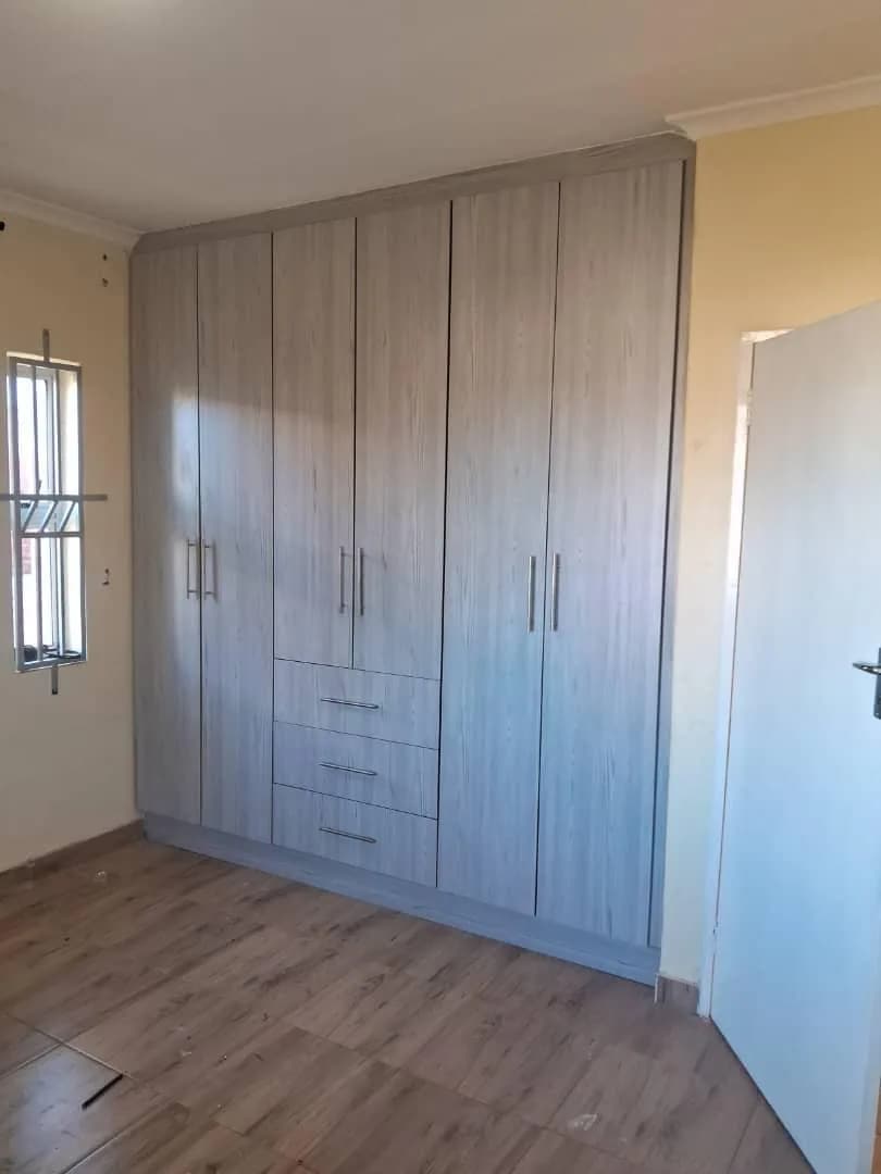 Floor-to-ceiling woodgrain built-in wardrobe with central drawers in a bedroom